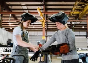 A woman welder helps a child put welding gloves on in a workshop